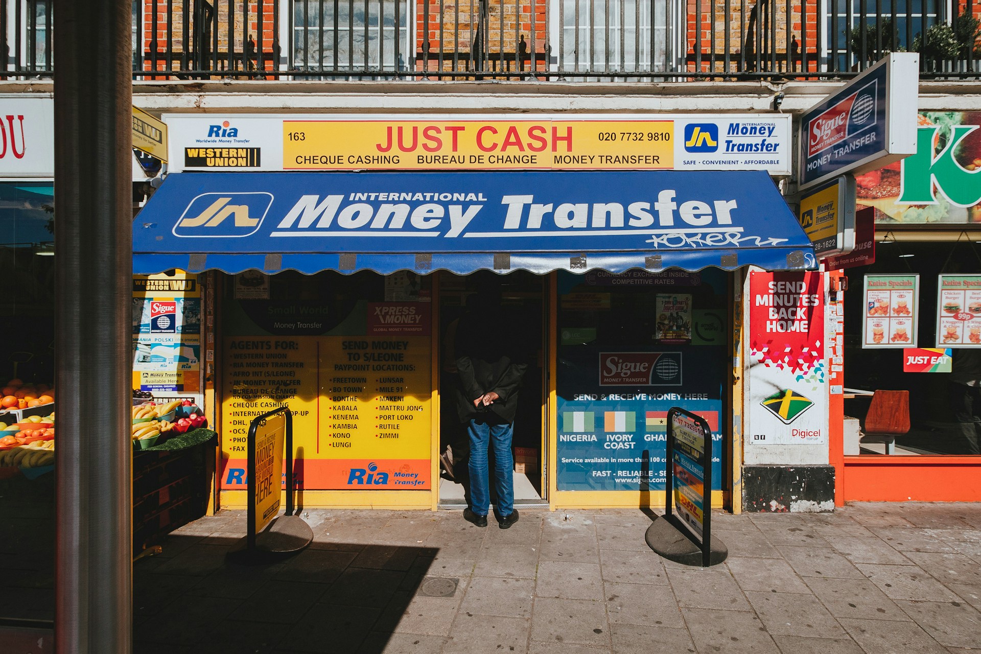 Street scene of a man waiting in line at a money transfer shop. Photo by Alistair MacRobert @ Unsplash
