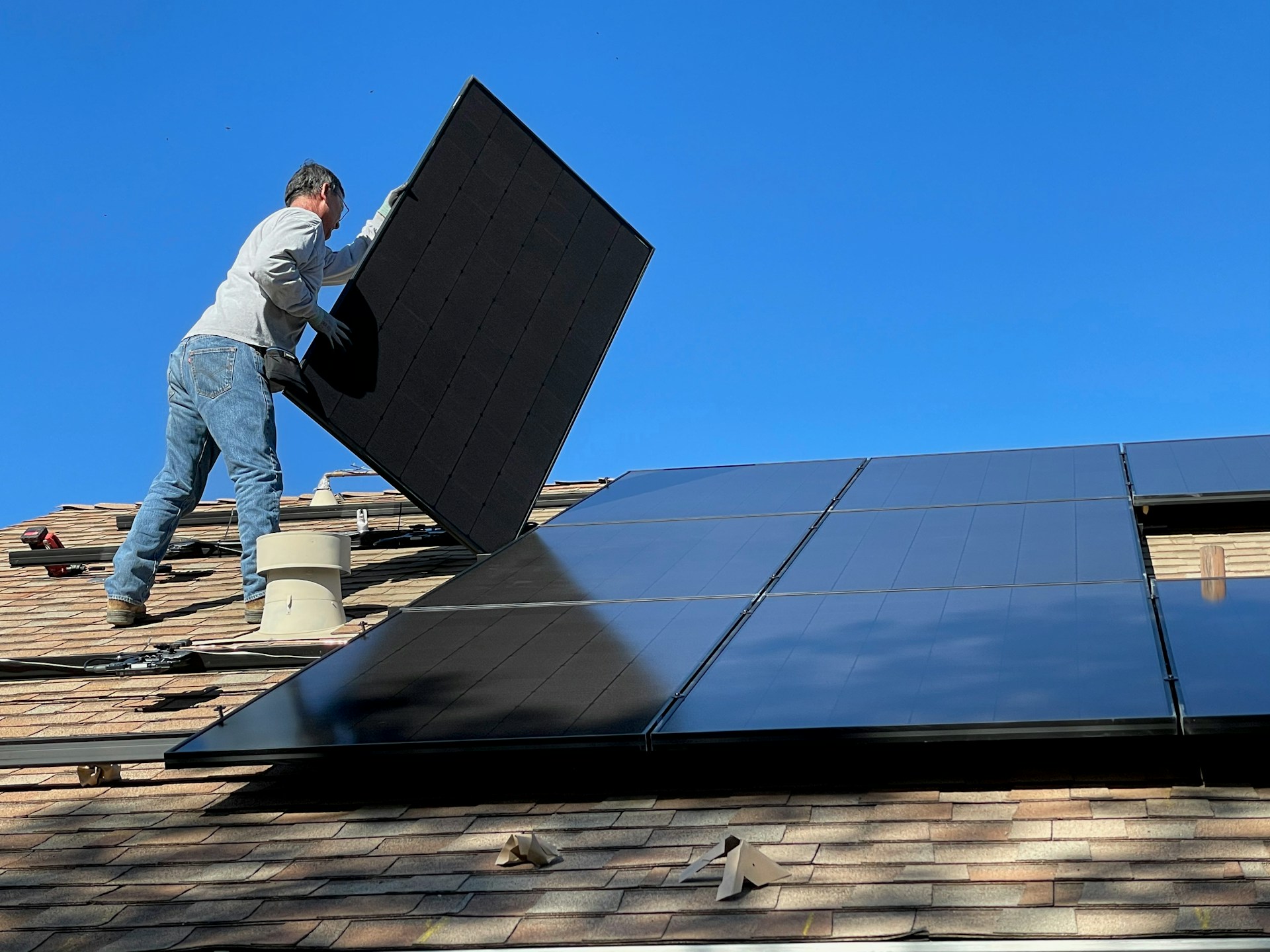 Worker installing solar panels on a roof. Photo by Bill Mead @ Unsplash