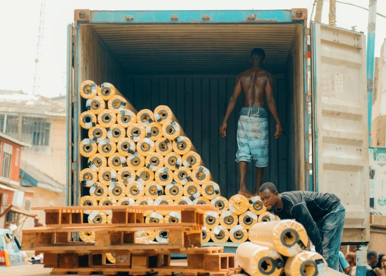 Men load rolls of fabric into a shipping container for export. Photo @Pexels