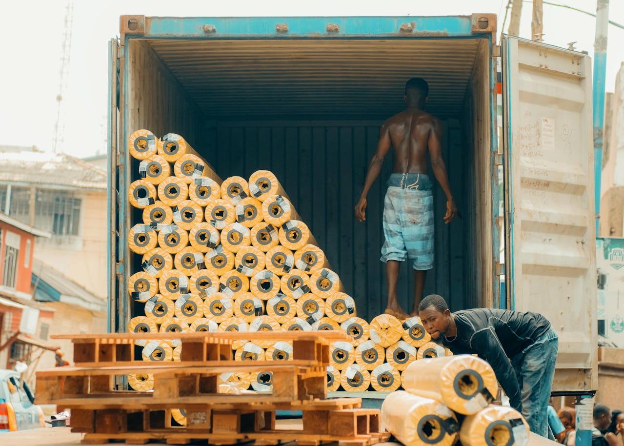 Men load rolls of fabric into a shipping container for export. Photo @Pexels