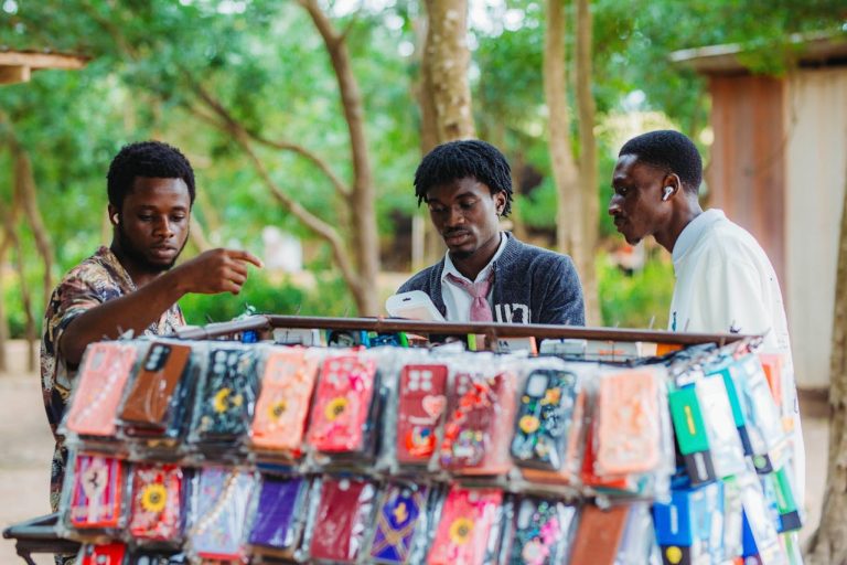 Three men browsing phone cases at an outdoor market stall in Accra, Ghana. Photo by Zeal Creative Studios @Pexels