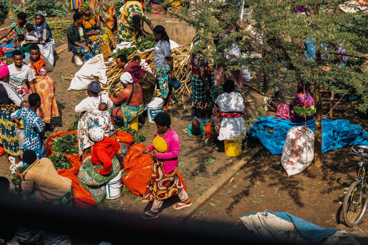 A bustling outdoor market in Africa with people engaged in trade and colorful textiles. Photo by Mad Knoxx Deluxe @ Pexels.