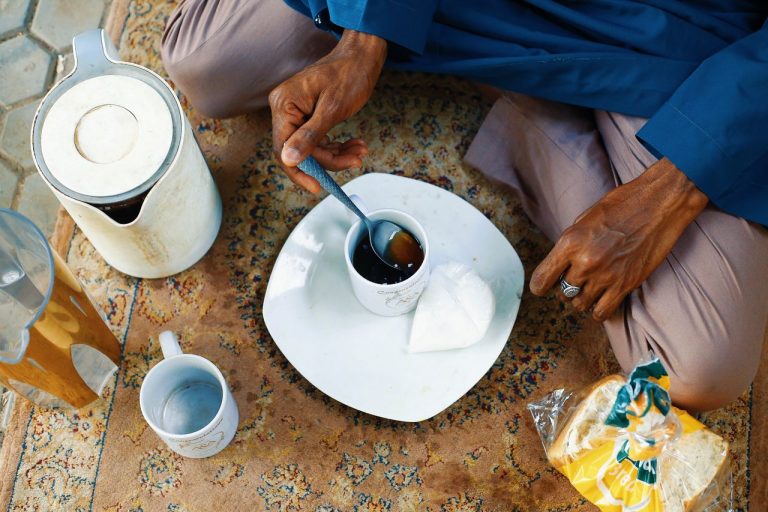 Hands preparing tea on a patterned rug with traditional bread and sugar in Abuja, Nigeria. Photo by Muhammad-Taha Ibrahim @Pexels