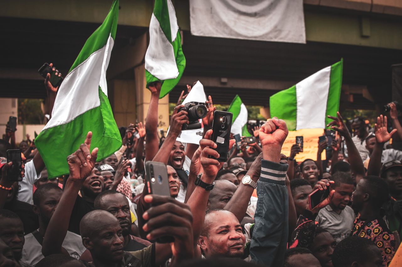 A lively street protest in Nigeria with activists waving flags and holding signs. Photo by Tope J. Asokere @Pexels